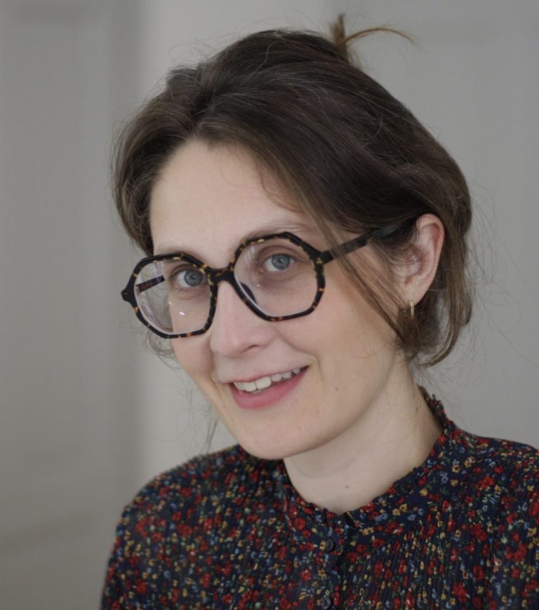 Portrait von Psychotherapeutin Silja Wübbelmann mit Brille und lockigem Haar, lächelnd in einem Raum.
